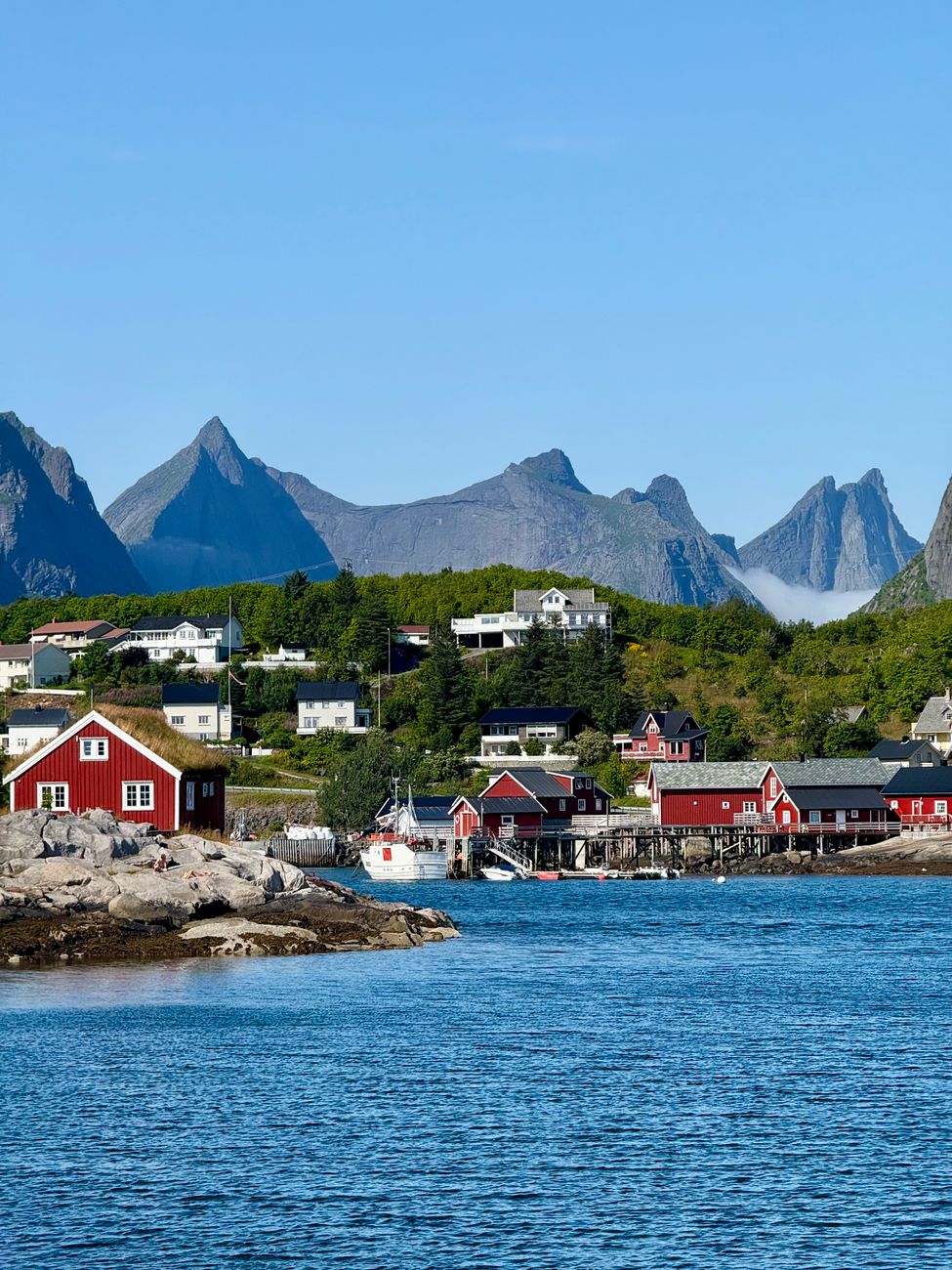 Traditional red wooden cabins on stilts over calm Arctic fjord waters